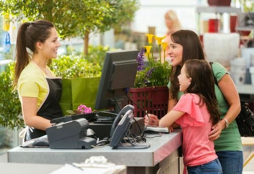 Une femme et sa fille à la caisse d'une jardinerie. La caissière est face à sa caisse et aux clients.