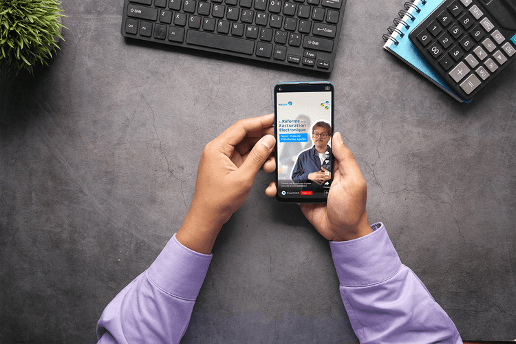Zoom sur des mains, vue du dessus, tenant un téléphone avec la vidéo de WeSoft sur le choix de la plateforme agréée concernant la réforme de la facturation électronique