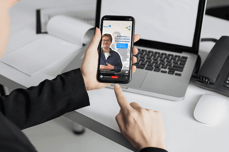 Zoom sur les mains d'un homme professionnel face à son bureau qui tient son téléphone pour regarder la vidéo de WeSoft sur la facturation électronique