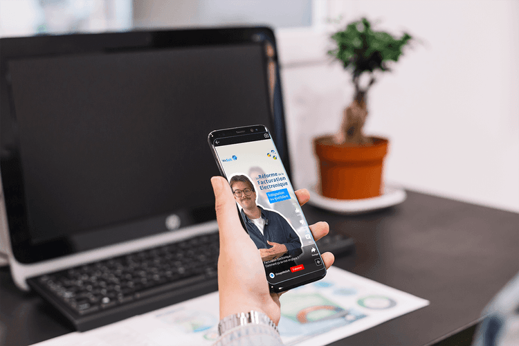 Vue de biais sur une main tenant un téléphone avec la vidéo sur l'offre commerciale proposée par le groupe WeSoft