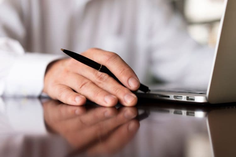 Zoom sur une main posée à côté de son ordinateur portable, tenant un stylo