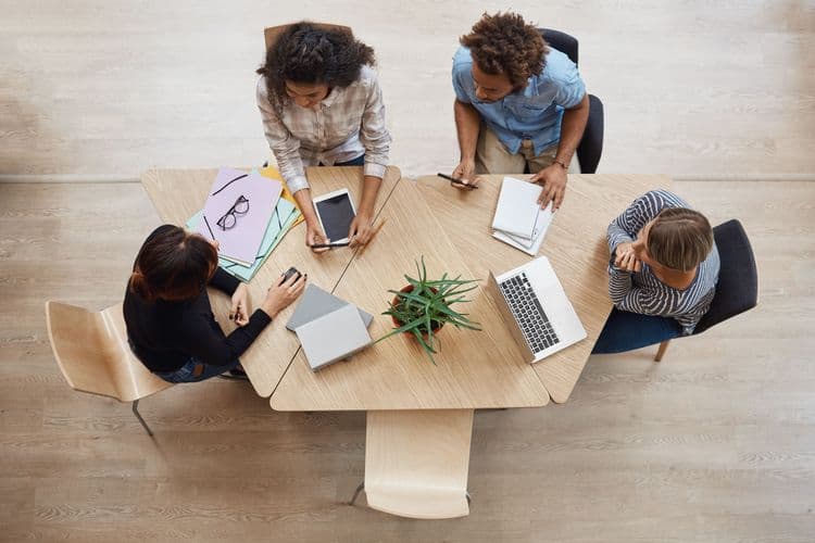 Vue de dessus de professionnels assis autour d'une table avec leurs ordinateurs, des notes, des dossiers et autres documents professionnels